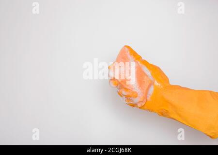 Main dans un gant en caoutchouc orange avec une éponge orange et de la mousse sur fond blanc. Lavage de vaisselle, nettoyage, nettoyage à la maison. Banque D'Images