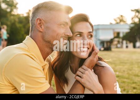 Portrait de joli couple homme et femme à côté à copyspace et s'étreindre alors qu'il était assis sur l'herbe en été park Banque D'Images