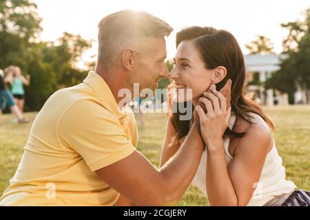 Portrait de joli couple homme et femme à l'un l'autre et s'étreindre alors qu'il était assis sur l'herbe en été park Banque D'Images