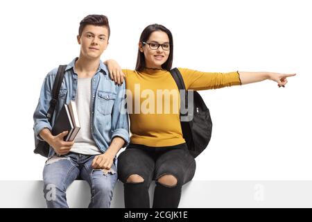 Étudiants assis sur un panneau et pointant vers le côté isolé sur fond blanc Banque D'Images