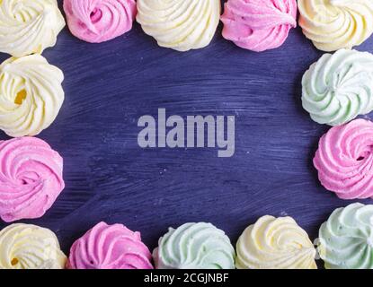 Cadre coloré de meringues multicolores sur fond en bois noir. Espace de copie, vue de dessus, plat. Banque D'Images