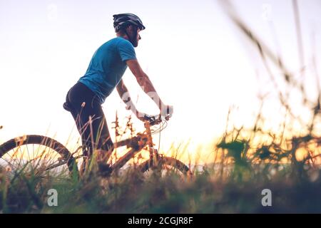 Homme cycliste homme rencontre un coucher de soleil en haut de la colline au-dessus de la ville. Image de concept de sport actif Banque D'Images