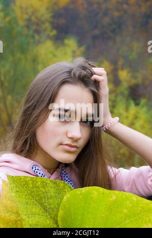 Automne nature fond. Jeune femme dans la forêt automnale. Belle adolescente fille avec de longs cheveux blonds et les yeux verts est tenue grand leav vert Banque D'Images