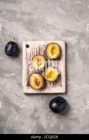 Fruits prune mûrs frais entiers et coupés en tranches sur une planche à découper en bois, fond en béton de pierre, vue du dessus Banque D'Images