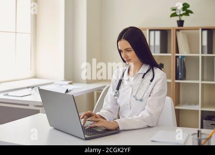 Jeune femme médecin dactylographiant sur ordinateur portable mot-clé surf net dans hôpital moderne Banque D'Images