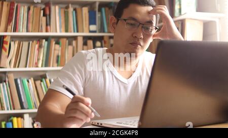 Asiatique musulman étudiant en bibliothèque, concept de préparation à l'examen. Étudiant d'université de sexe masculin faisant des recherches et utilisant un ordinateur portable pour apprendre en ligne Banque D'Images
