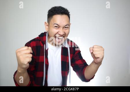 Un jeune homme asiatique couronné de succès montre un geste gagnant, célébrant la victoire. Les mains soulevées au-dessus avec l'omnigramme expressif wow Happy face Banque D'Images