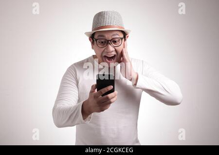 Beau jeune homme asiatique lisant des SMS bavardant sur son téléphone, choqué expression surprise Banque D'Images