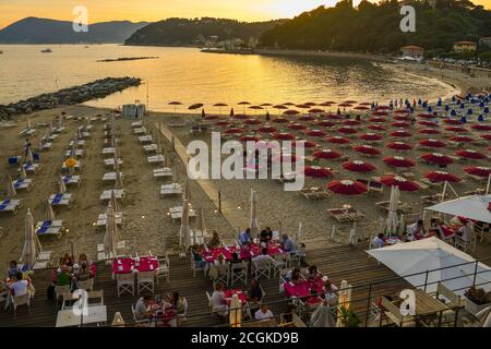 Vue imprenable sur les personnes dînant dans un restaurant en plein air donnant sur une plage de sable dans le golfe de Poets au coucher du soleil, San Terenzo, la Spezia, Italie Banque D'Images