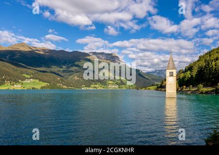 L'ancien clocher submergé du lac Resia à Val Venosta, Tyrol du Sud, Italie, émerge de l'eau sur un beau ciel bleu avec du clou blanc Banque D'Images