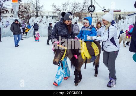 Un enfant est à cheval sur un poney intelligent en arrière-plan un parc d'attractions de glace dans le centre de Krasnoyarsk pendant les vacances de Noël. Krasnoyarsk Territo Banque D'Images