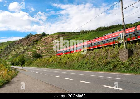 Un train de voyageurs rouge longeant une autoroute vide à côté des collines d'un vignoble en Allemagne. Banque D'Images