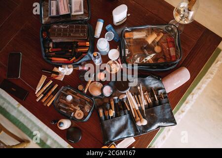 Kit maquilleur. Pinceaux de maquillage, poudre, brillant à lèvres, fard à joues et autres cosmétiques sur une table en bois dans une salle avec un verre de vin. Banque D'Images