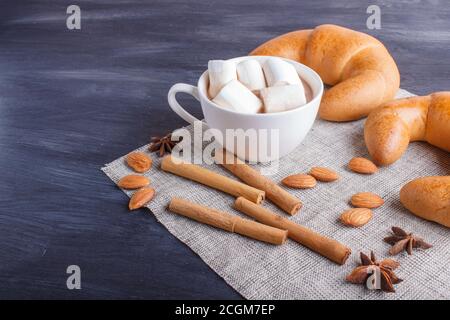 une tasse de chocolat chaud avec guimauve, croissants et épices sur serviette en lin et fond en bois noir. gros plan, espace copie. Banque D'Images