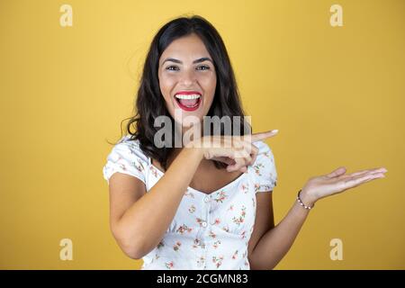 Belle femme sur fond jaune surpris, montrant et pointant quelque chose qui est sur sa main. Banque D'Images