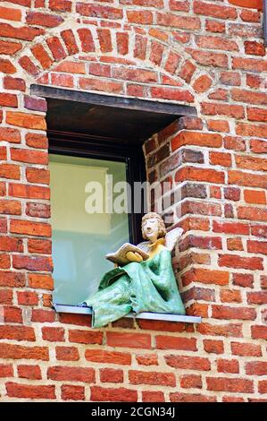 Un ange lisant un livre perché sur le seuil de la fenêtre à l'extérieur d'un bâtiment à Torun, en Pologne. Banque D'Images