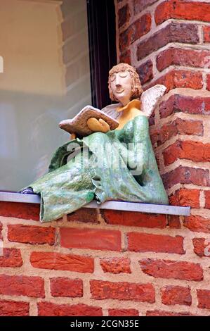 Un ange lisant un livre perché sur le seuil de la fenêtre à l'extérieur d'un bâtiment en briques dans la vieille ville de Torun, en Pologne. Banque D'Images