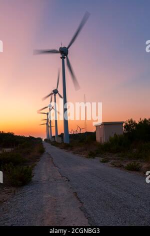 Gros plan sur les éoliennes du parc éolien de Bozcaada. Le tir à longue exposition capture les turbines lorsqu'elles tournent. Une route de terre et un buil de transformateur Banque D'Images