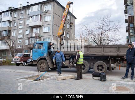 Écologisation de la ville de Krasnoyarsk. Les travailleurs sont engagés dans la plantation d'un arbre, amené par camion, dans une zone résidentielle sur fond de maisons. Banque D'Images
