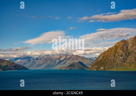 Vue sur la montagne et le lac Hawea. En été, il y a de l'herbe verte et des cieux bleus avec de beaux nuages au cou, Otago, Nouvelle-Zélande. Banque D'Images