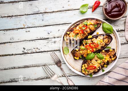 Bateaux d'aubergines cuits au four, farcis de viande hachée, tomates, maïs, ail et fromage en plaque blanche, vue de dessus Banque D'Images