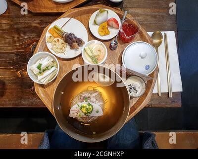 Divers types de plats traditionnels coréens sont mis sur table. Pyongyang naengmyeon, soupe réfrigérée de nouilles de sarrasin. Racine de lotus frite et poitrine grillée. Banque D'Images