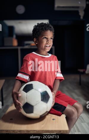 Un petit joueur de football dans un vestiaire se posant prêt pour une formation Banque D'Images