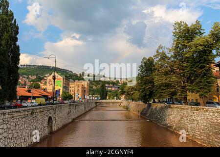 Sarajevo, Bosnie-Herzégovine - 3 juillet 2018 : la rivière Miljacka qui traverse Sarajevo en soirée d'été, avec un arc-en-ciel en arrière-plan, Banque D'Images