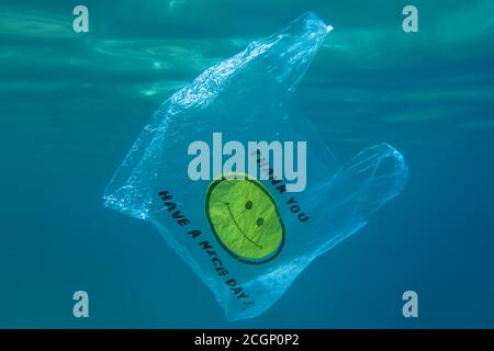 Un sac en plastique avec un visage jaune smiley et les mots merci, bonne journée! Flottant lentement sous l'eau dans l'eau bleue, Becici, région de Budva Banque D'Images
