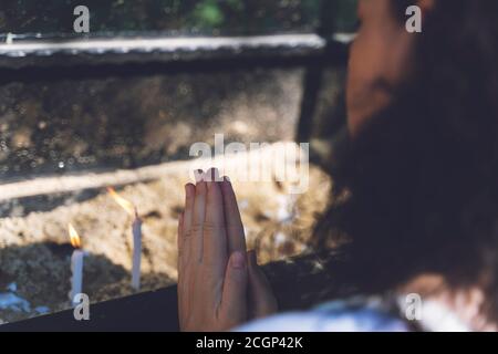 Femme priant et brûlant des bougies dans le jardin de la maison de la Vierge Marie. Bougies blanches allumées sur le support. Culte Banque D'Images