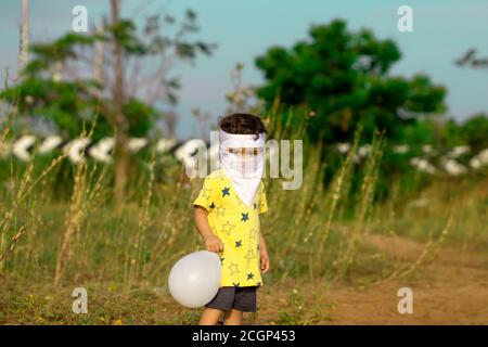 Pour éviter le virus corona, un petit enfant couvert d'une bouche pleine de masques faits maison de visage joué avec ballon dans le stationnement par la route ecr en c Banque D'Images