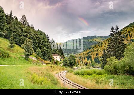 Chemin de fer dans une vallée pittoresque des Alpes. Partie d'un arc-en-ciel au-dessus des montagnes. Banque D'Images