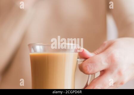 femme en chandail beige tenant une tasse de verre avec du café Banque D'Images
