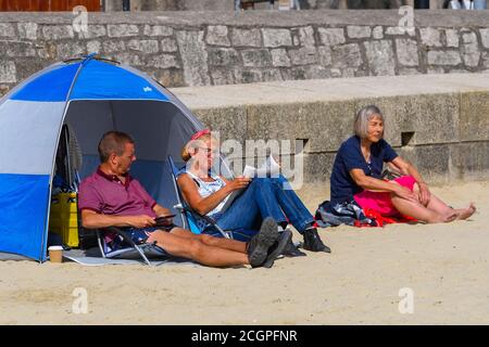 Lyme Regis, Dorset, Royaume-Uni. 12 septembre 2020. Météo Royaume-Uni. Bains de soleil se détendre sur la plage lisant un journal à la station balnéaire de Lyme Regis à Dorset un matin de soleil brûlant au début d'une mini vague de chaleur. Crédit photo : Graham Hunt/Alamy Live News Banque D'Images