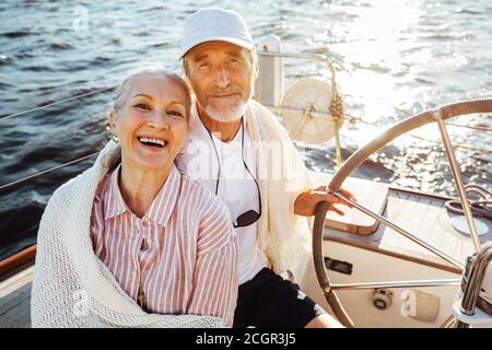 Couple senior assis au volant sur un voilier et regarder l'appareil photo Banque D'Images