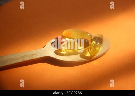 capsules de gel oméga d'huile de foie de morue dans une cuillère en bois sur fond orange. Concept de soins de santé Banque D'Images