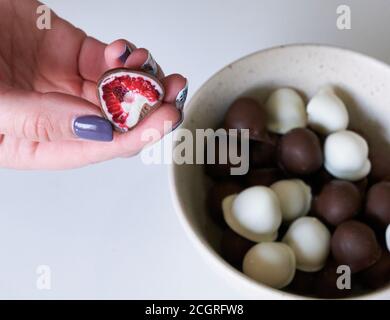 la main de femme choisit et attrapant rouge frais et brillant frais framboises enrobées de chocolat noir et blanc fait maison Banque D'Images