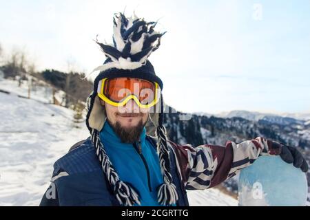 Drôle de barbu homme Snowboarder portrait en chapeau mohawk aime le station de ski dans les montagnes Banque D'Images