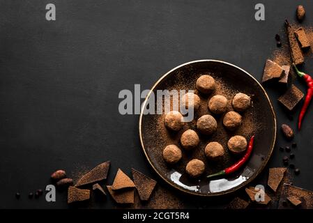 Truffes au chocolat faites maison sur l'assiette avec piments et morceaux de chocolat, fond noir, vue du dessus, espace de copie. Banque D'Images