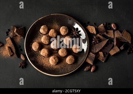 Truffes au chocolat faites maison sur l'assiette et morceaux de chocolat écrus sur noir, vue du dessus, espace de copie. Banque D'Images