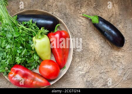 La tomate rouge, le poivre, le persil, l'aubergine sont sur une assiette en bois sur fond marron. Ingrédients pour cuisiner. Vue du dessus Banque D'Images