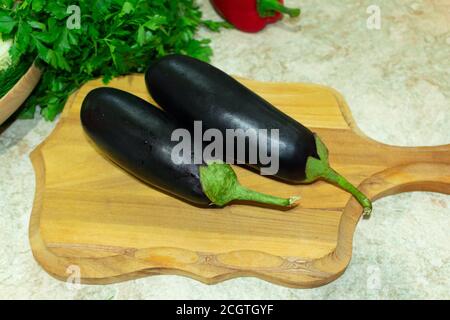 deux aubergines sur une planche de bois à côté du persil et poivron rouge Banque D'Images