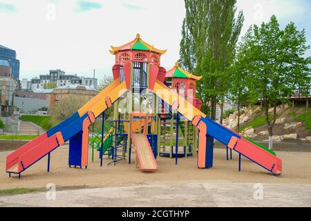 Terrain de jeu coloré pour enfants sur une cour de sable à proximité de beaux bâtiments. Banque D'Images