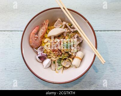 Nouilles dans un bol, avec crevettes, calmar, piment et légume, sur une table en bois, fond flou Banque D'Images