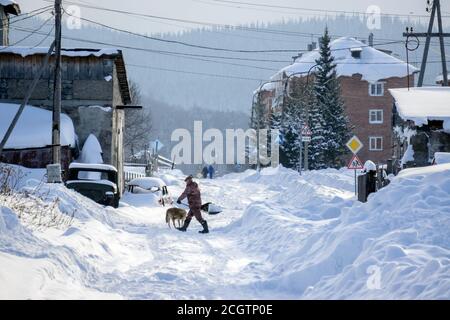 Homme avec une pelle nettoie la neige à la périphérie du village sur le fond des bâtiments résidentiels. Banque D'Images