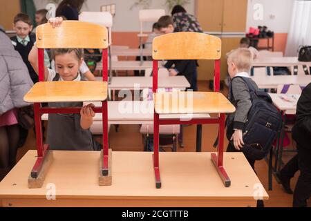 Les premiers interprètes mettent des chaises sur le bureau à la fin des cours à l'école primaire rurale. Banque D'Images