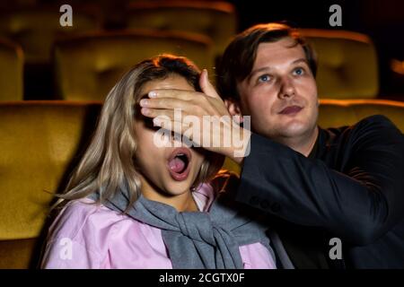 Un couple regardant un film thriller dans le cinéma, les hommes utilisent leurs mains pour fermer les yeux de sa petite amie. Banque D'Images