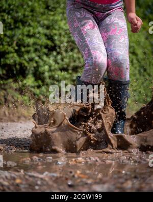 Une jeune fille sautant dans une flaque boueuse et de l'eau brune éclabousser tout autour d'elle Banque D'Images