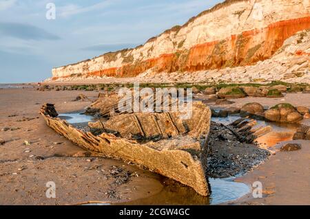 Le soir, la lumière du soleil sur l'épave du chalutier à vapeur Sheraton, sous les falaises rayées rouges et blanches de Hunstanton à marée basse. Banque D'Images