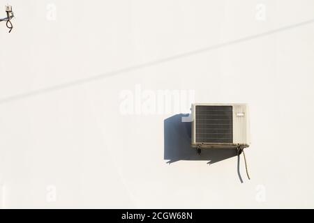 Ancienne machine de climatisation installée sur un mur blanc, avec une forte lumière du soleil de milieu de journée Banque D'Images